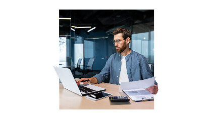 muž s papierom v ruke pracujúci na notebooku